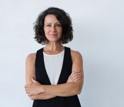 A mature woman with curly black hair crossing her arms